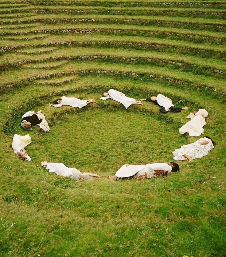 Aerial view of people in white lying in a circle formation on grass within a stone amphitheater